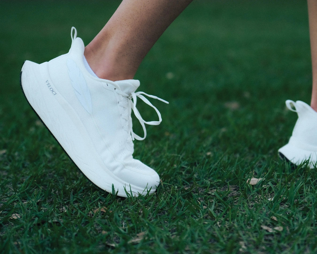Side view of the Veloci Ascent pair in white displaying the spacious toe box and lacing system, grassy outdoors