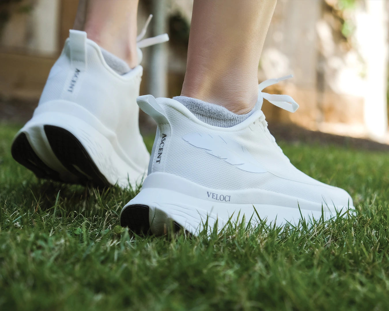 Rear view of the Veloci Ascent pair in white displaying the elevated heel drop, grassy outdoors