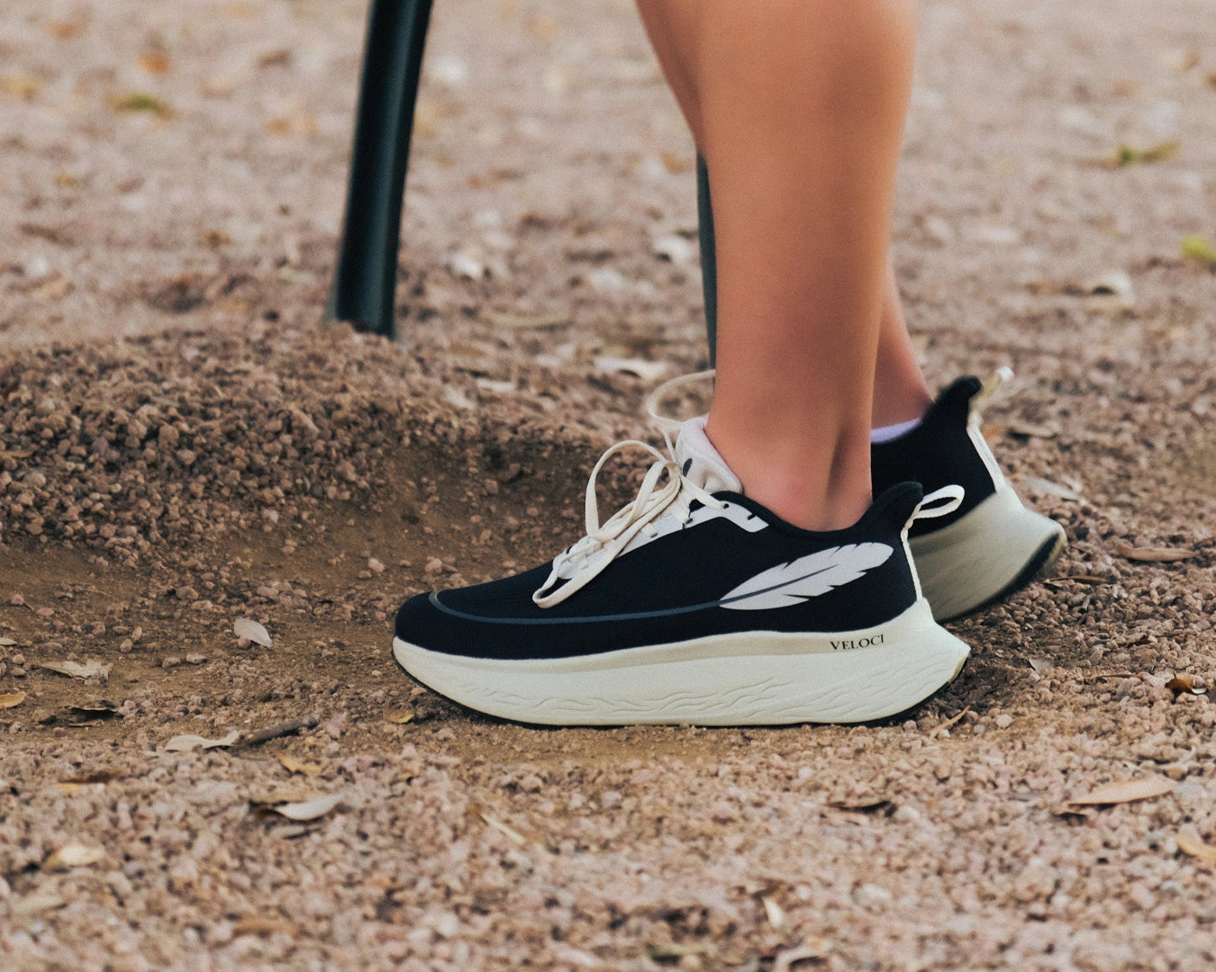 Veloci Ascent running shoe in black with cream midsole, outdoor gravel side profile showing the supportive foam, wide toe box and breathable mesh upper