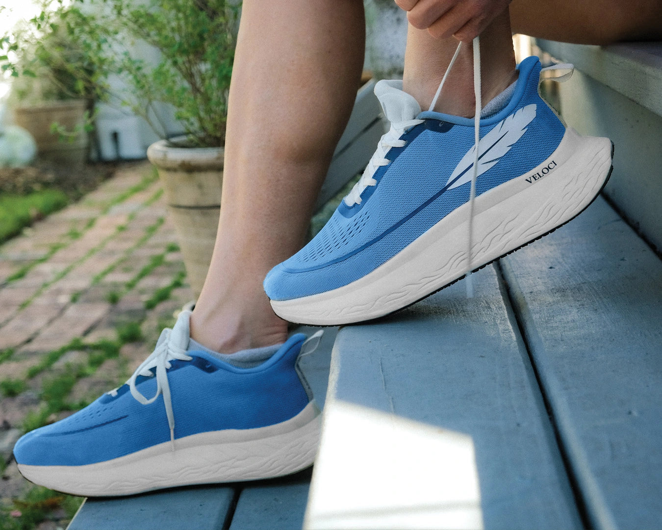Veloci Ascent running shoe in blue with white midsole, side profile showing the supportive foam and breathable mesh upper, outdoor staircase