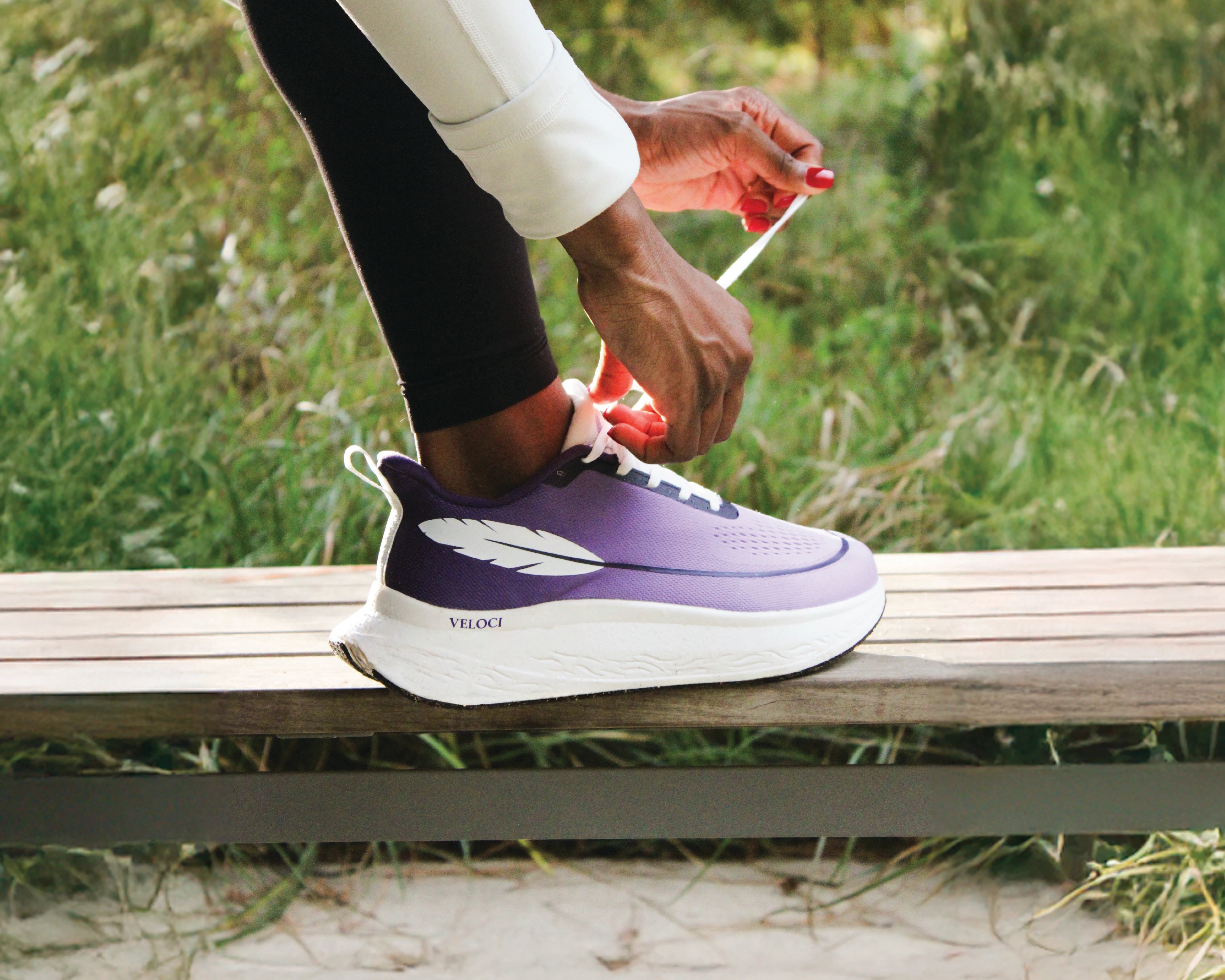 Person tying a purple and white sneaker with 'Veloci' branding, sitting on a bench outdoors.