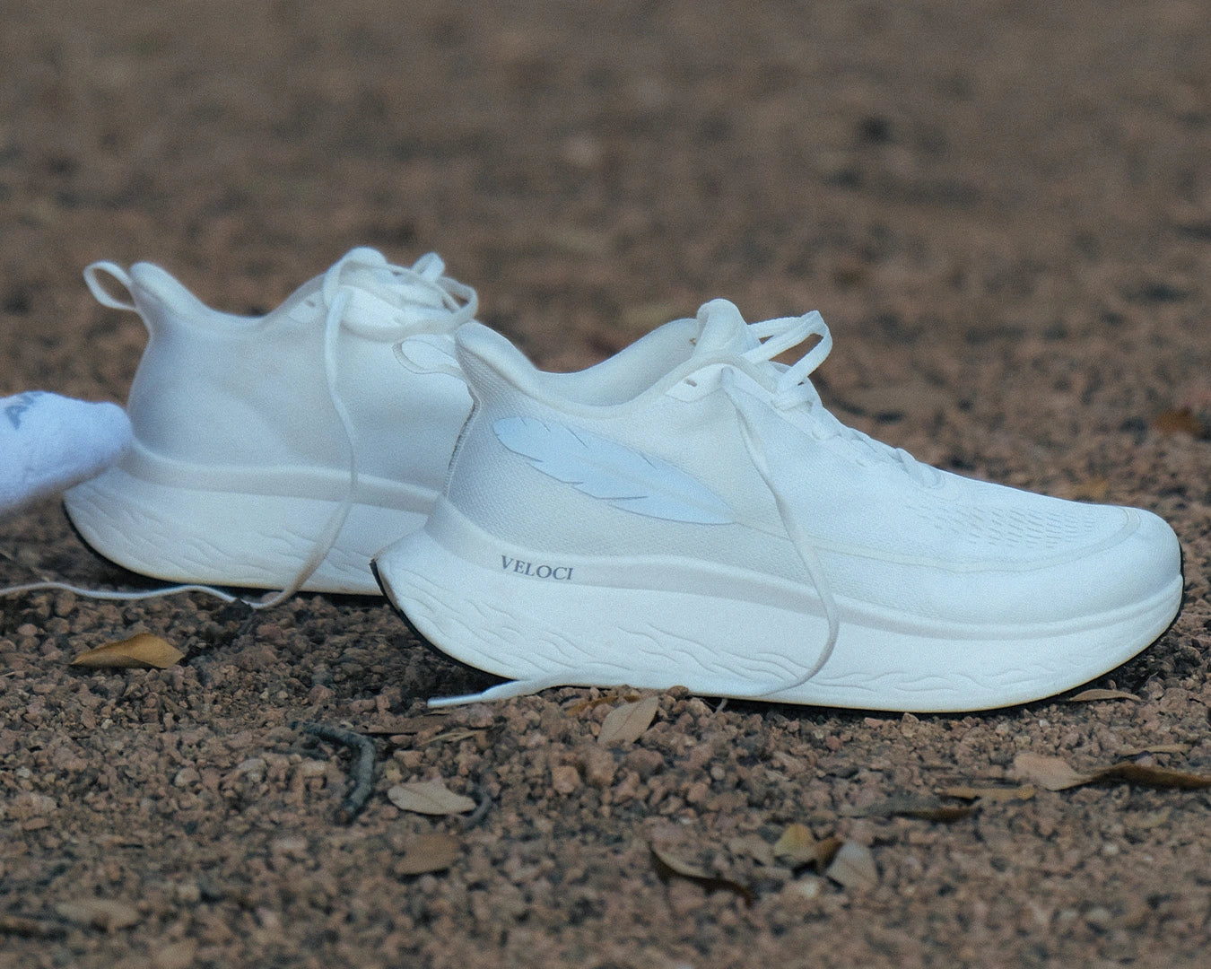 Side view of the Veloci Ascent pair in white displaying the spacious toe box and feather, gravel outdoors